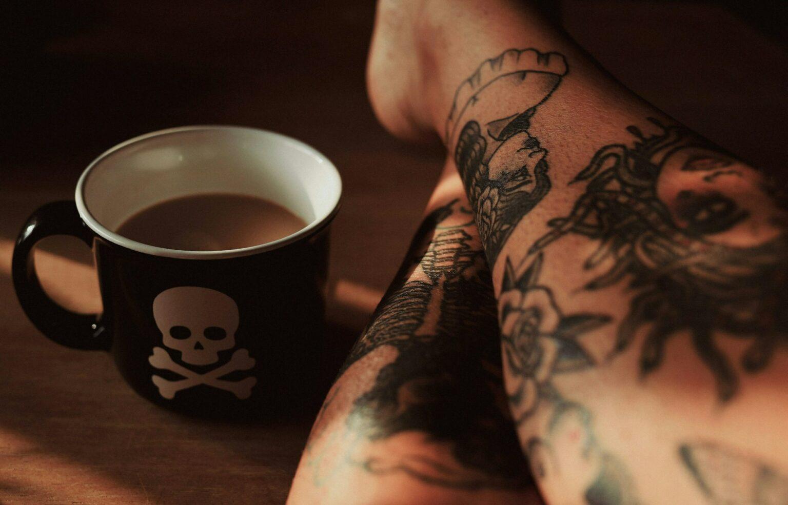 Ce que le tatouage dit de nous : une exploration psychologique Closeup shot of legs with tattoos with a skull bones cup full of coffee