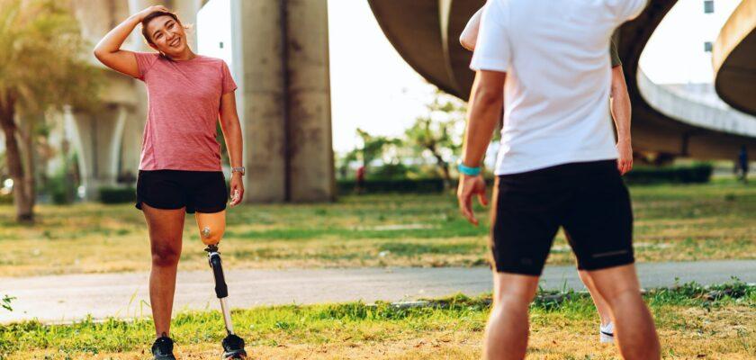 Friend support Friend with a prosthetic leg while exercising outdoor.