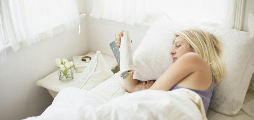 Blonde woman reading in a bed with white linen.