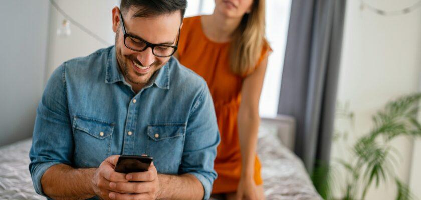 Jealous woman spying boyfriend and watching his mobile phone. Couple cheating jealousy concept