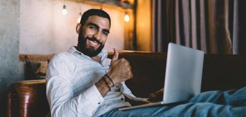 Man with laptop sitting on sofa and showing approve gesture