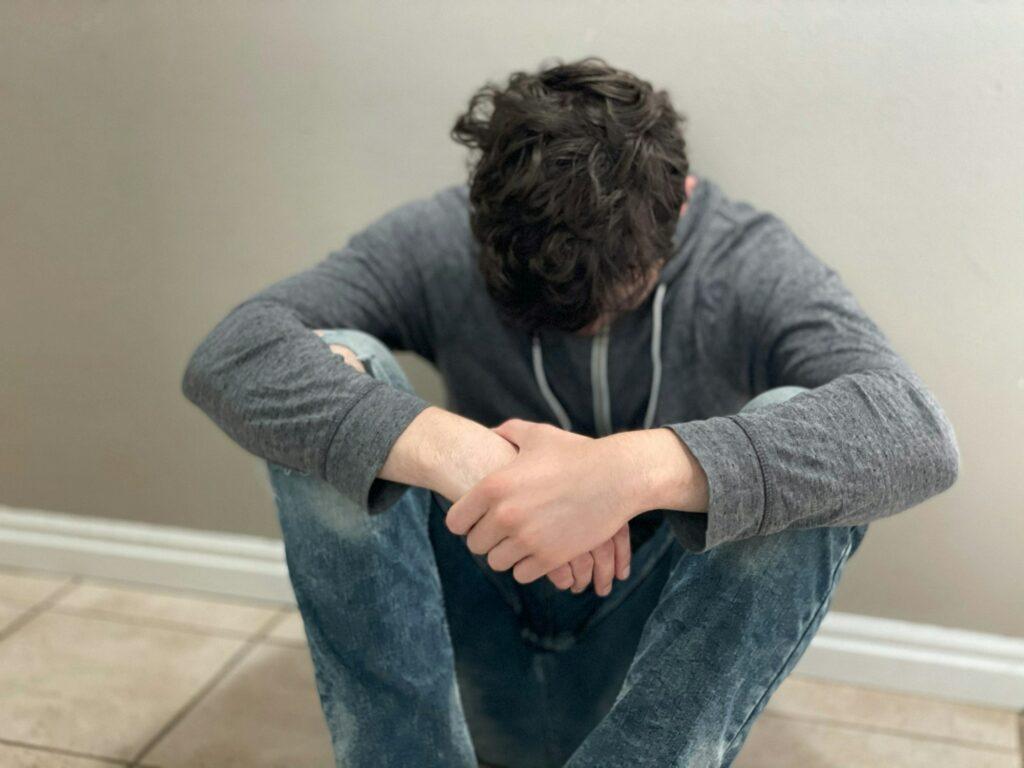 Teenage boy sitting alone head down, emotion concept. Embarrassed, sad, depressed mood, shame.