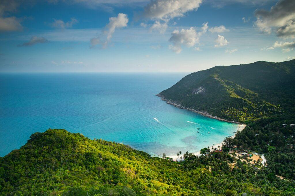 Thailand jungle island aerial: ocean sand beach at resort lodges, homes, cottages at spring forest