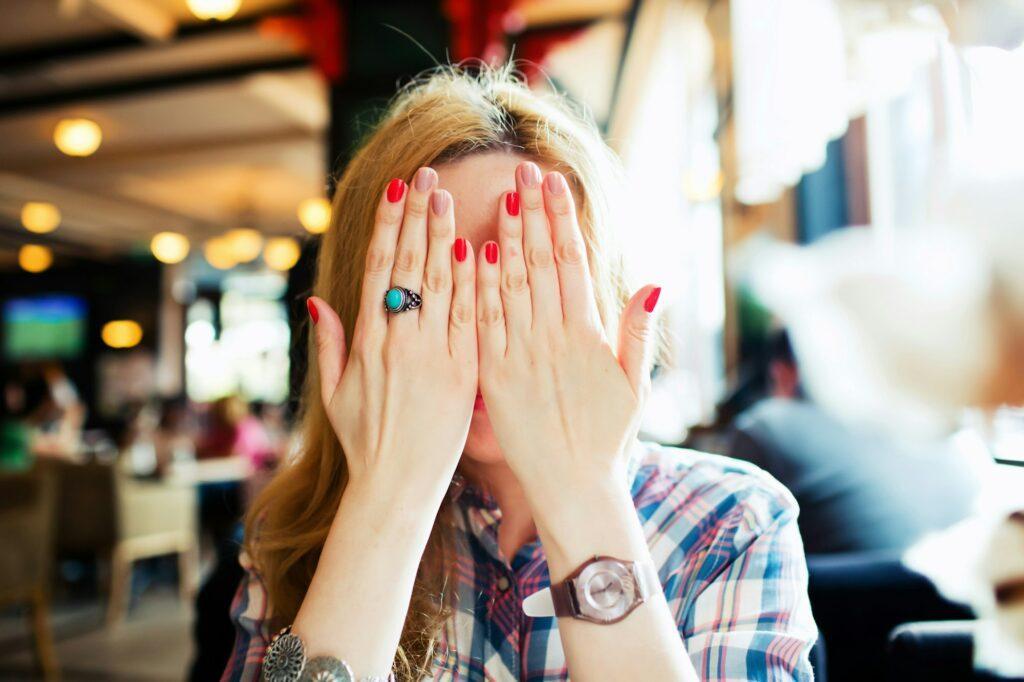 Young shy woman close her face by hand