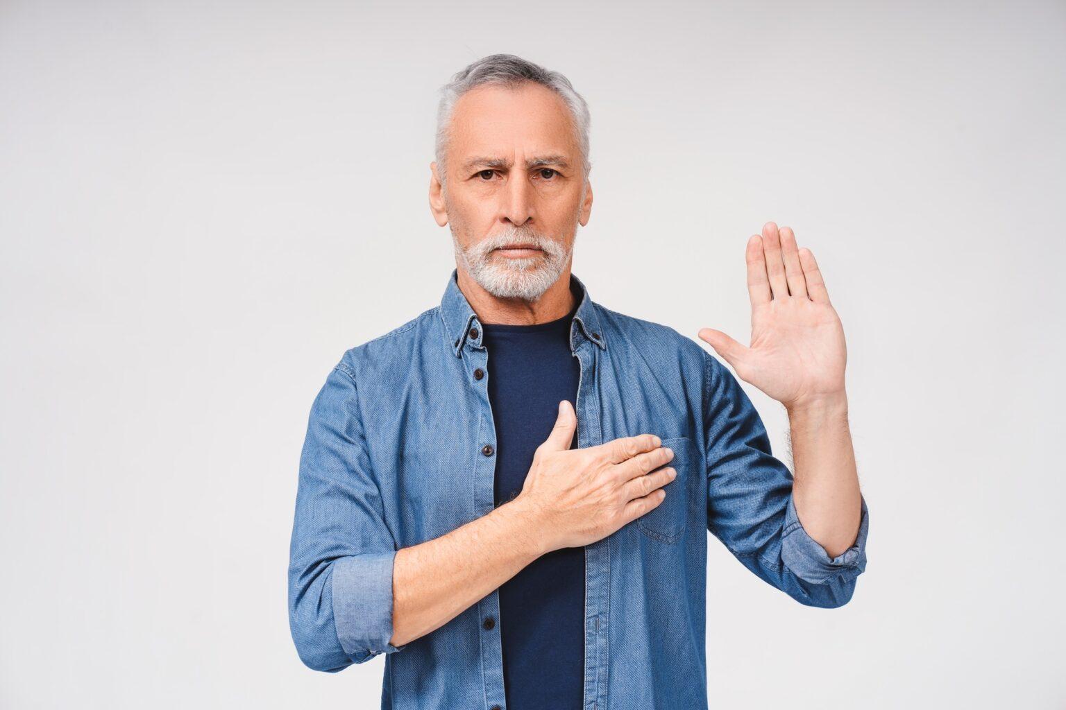 Mature man with grey hair making a loyalty promise oath, posing in studio, isolated on white