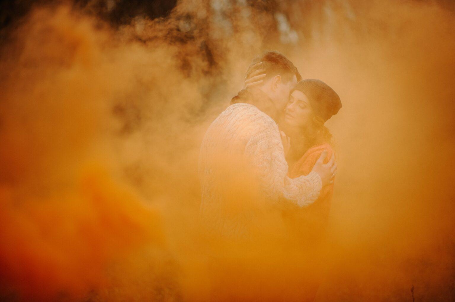 Young happy couple holding smoke bombs on camping