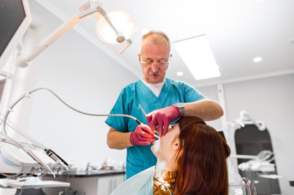 Senior male dentist working with his young patient woman visiting dentist