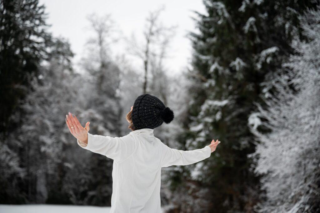 Young woman standing in snowy nature with her arms spread widely