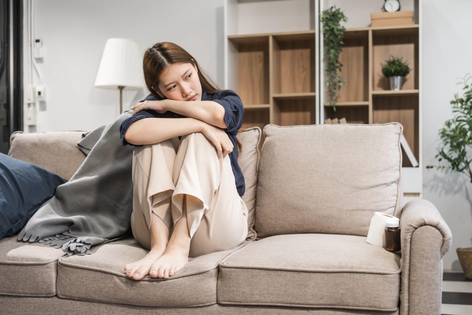 Anhédonie : les symptômes, les causes et le traitement A young female Asian is sitting on a sofa, showing signs of depression. She looks sad and hopeless