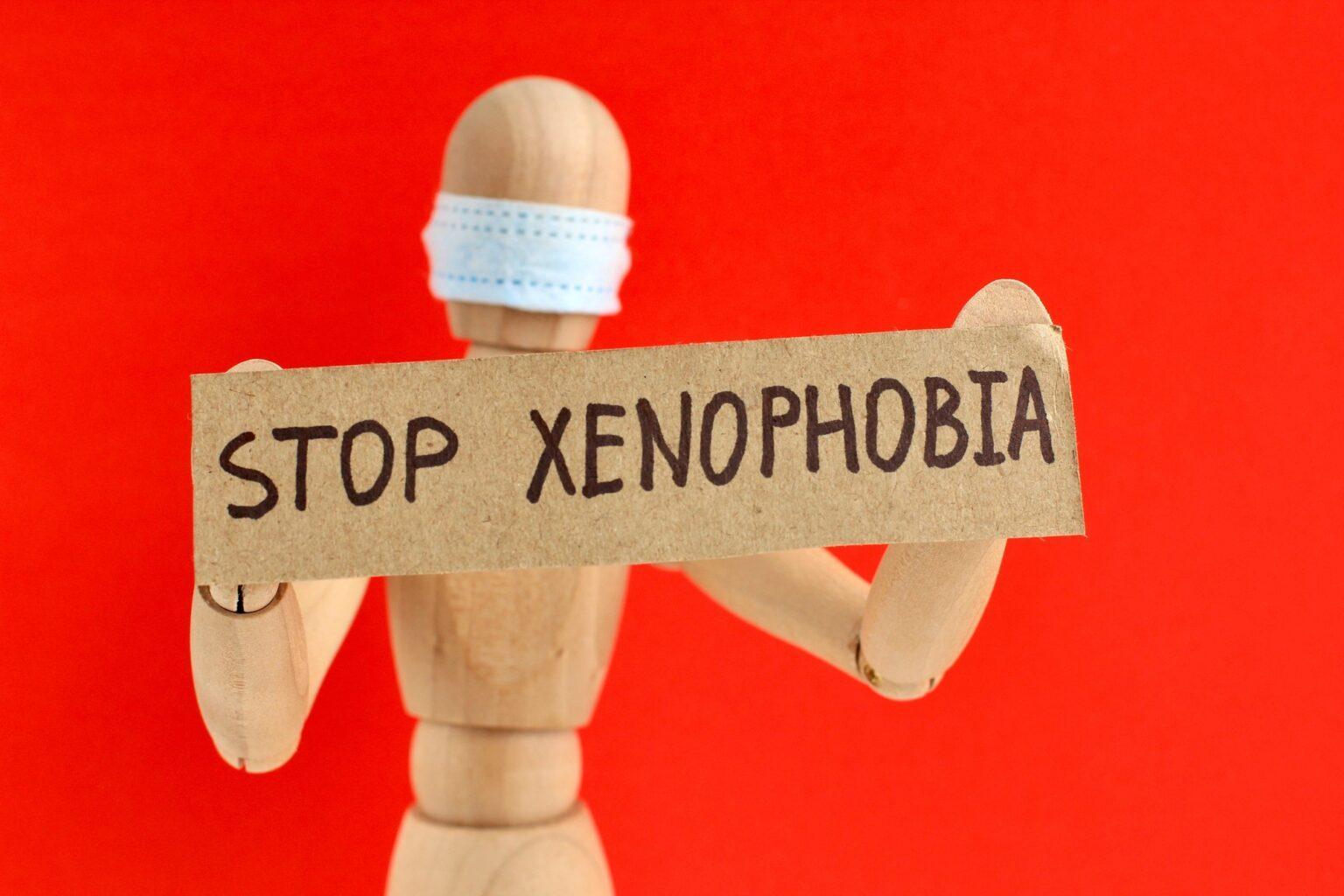 Symptômes de la xénophobie Cardboard sign with text stop xenophobia in the hands of mannequin in a medical mask. Anti racism.