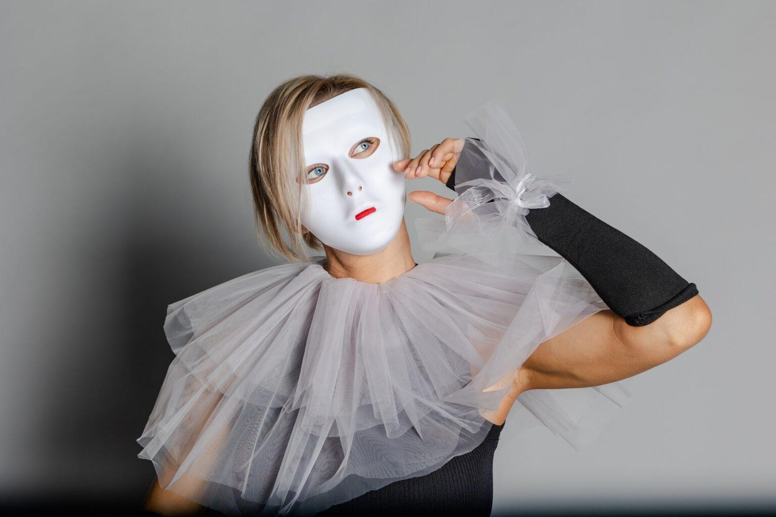 Woman in white theater mask and harlequin collar on gray background. Fancy dress, masquerade clothes