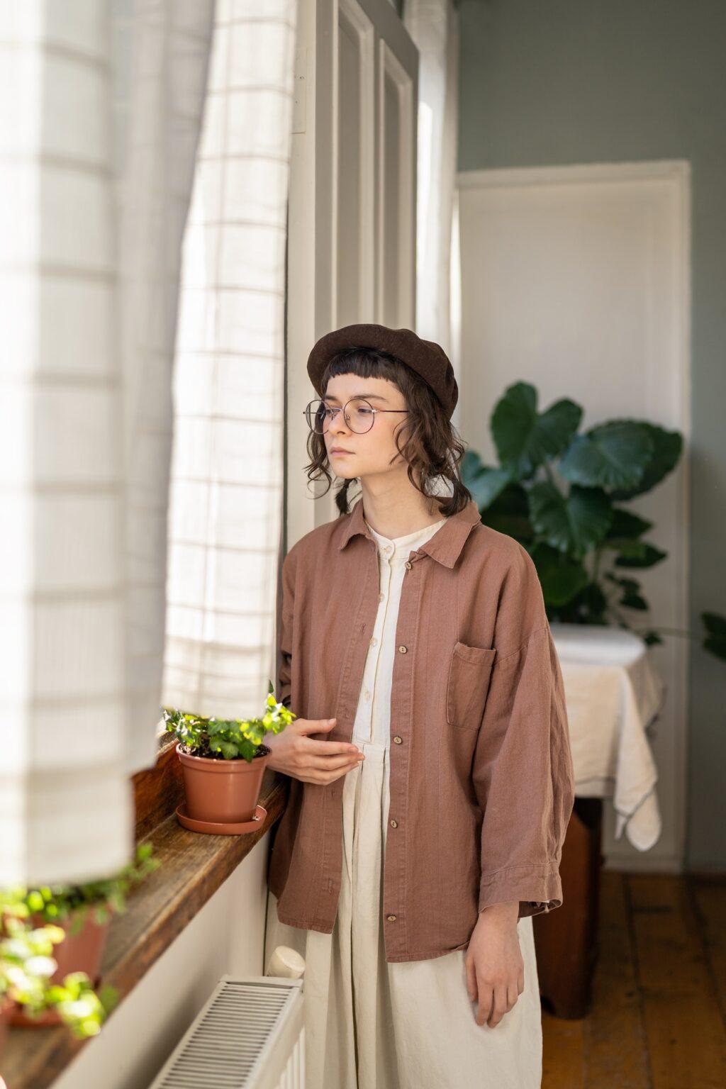 Pensive introvert young woman spy from behind curtain into window on neighbours. Social phobia