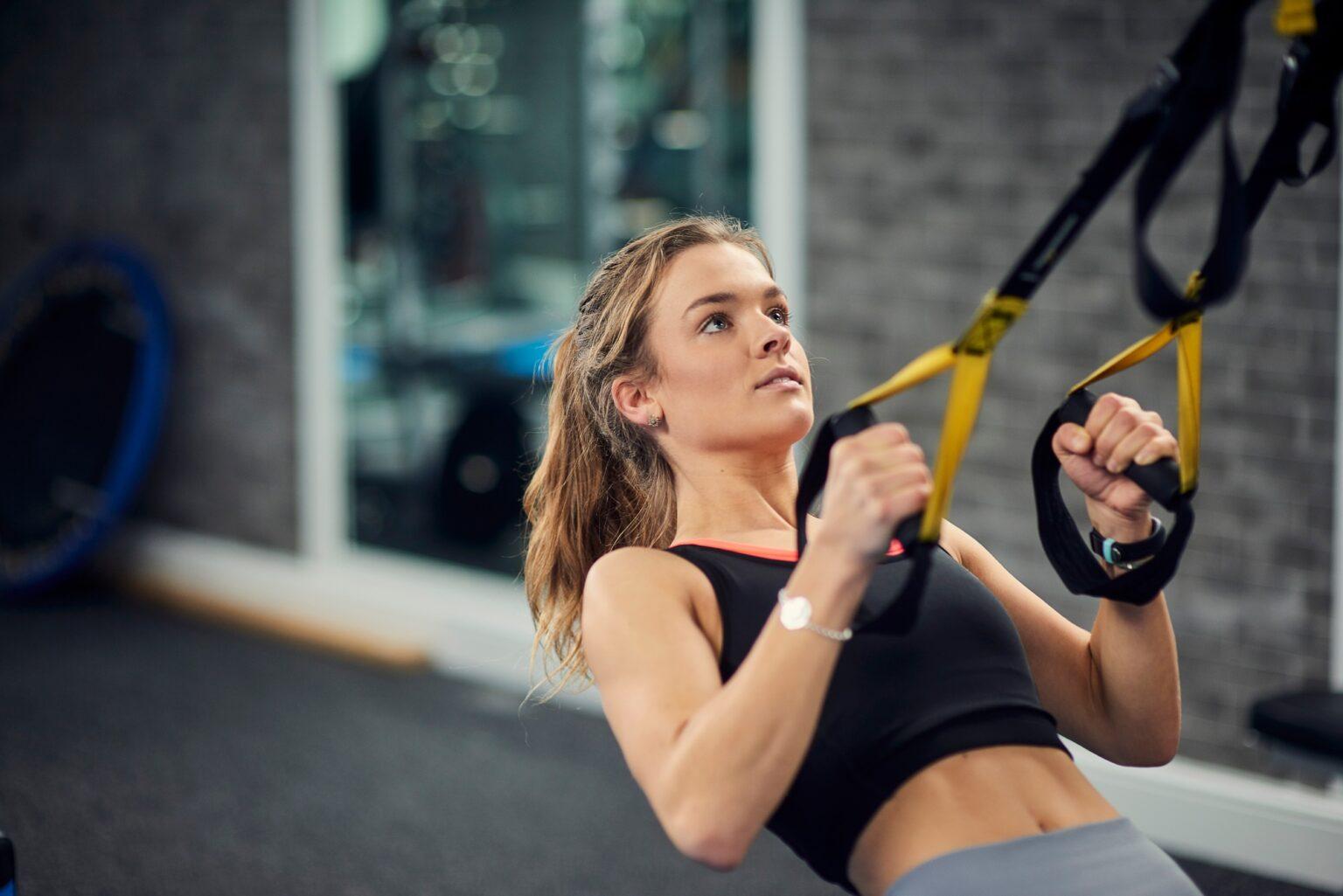 Young woman doing pull ups on exercise handles in gym