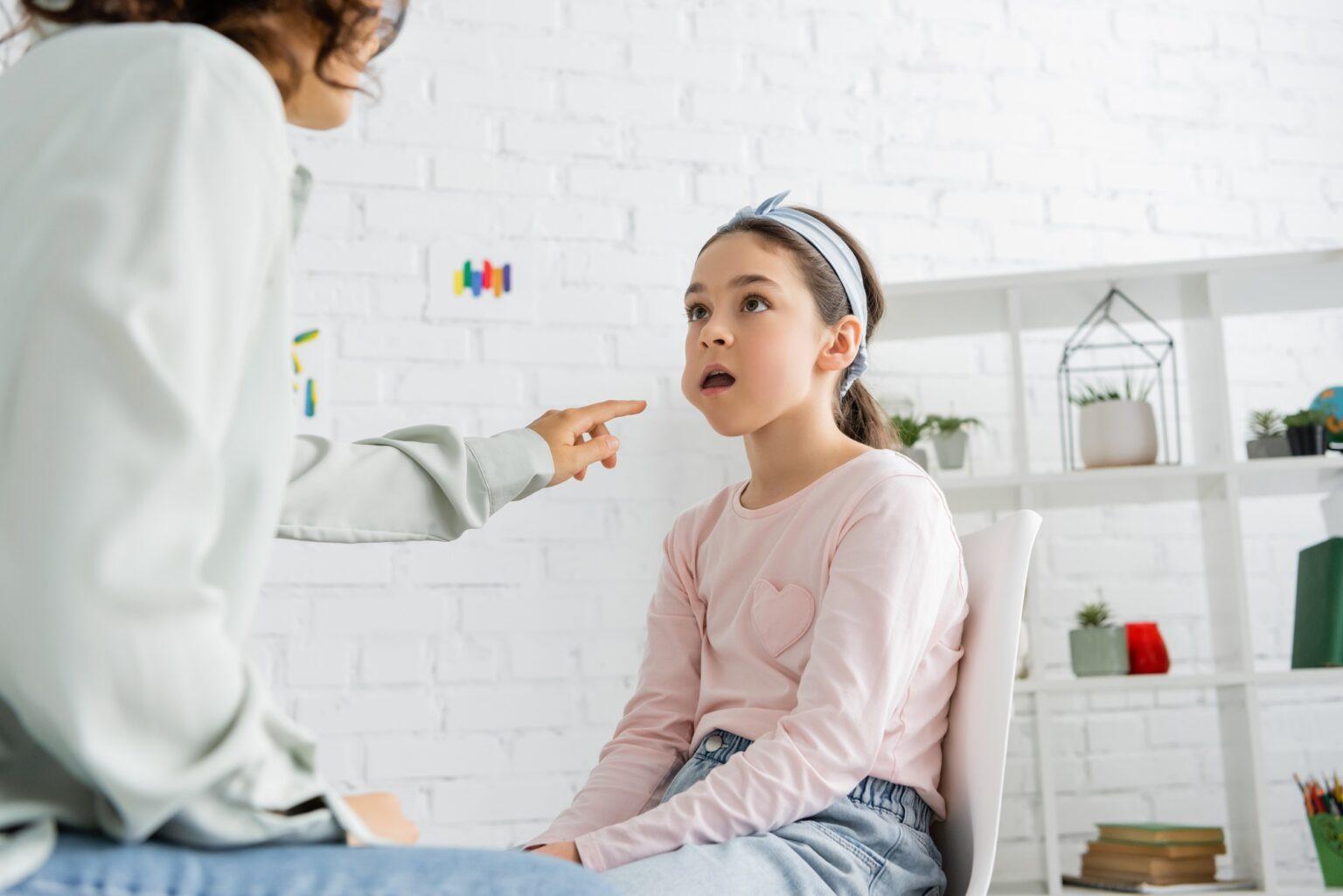 Bredouillement : comprendre ses causes et comment y remédier Speech therapist pointing at cheek of preteen girl in consulting room