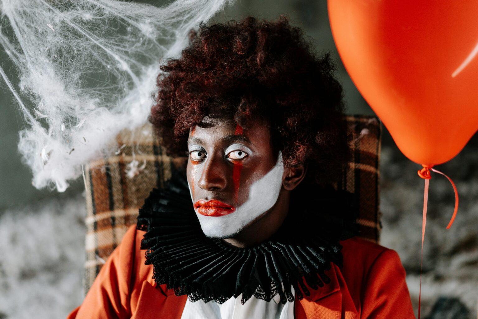coulrophobie : comprendre la peur des clowns et ses impacts Spooky clown face with dramatic makeup, holding a red balloon amidst cobwebs. Halloween vibe.