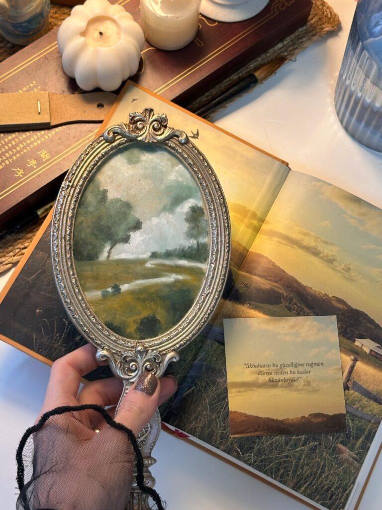 Comprendre le trouble thesaurisation : causes et effets sur la communication A vintage oval mirror held over an open book reveals a pastoral painting. Elegant decor setup.