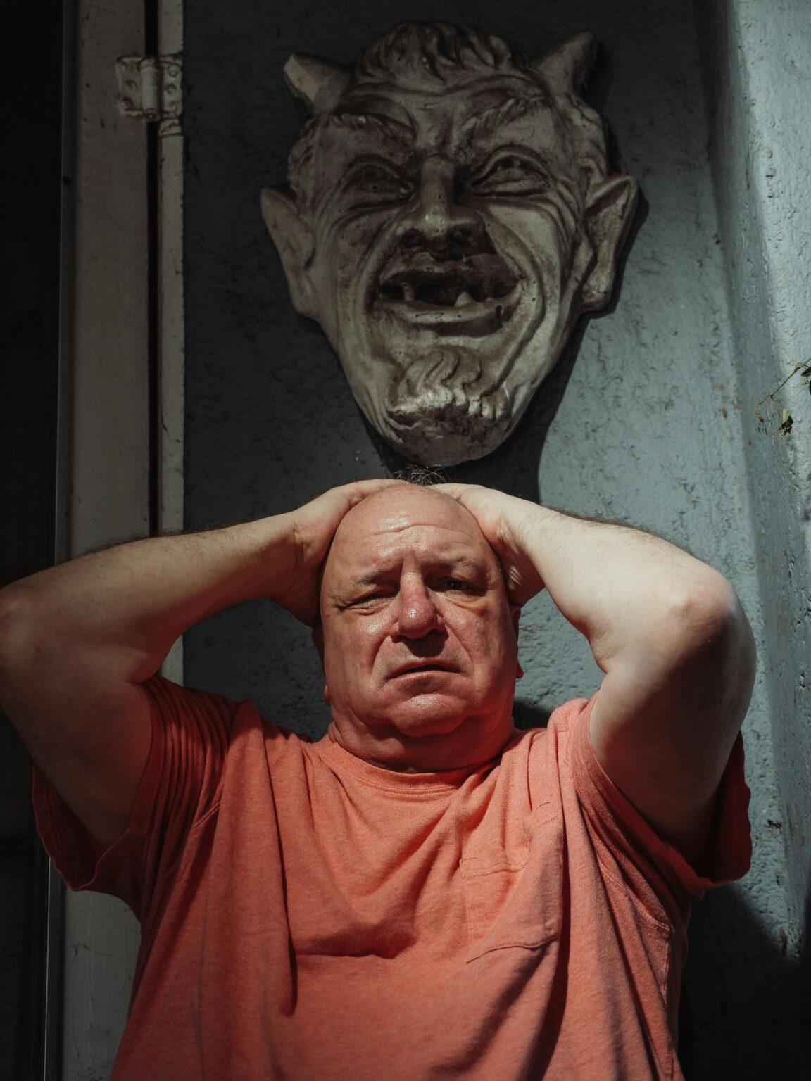 stasobasophobie : comprendre cette peur spécifique pour mieux la surmonter Elderly man with hands on head beneath a shadowy mask, feeling anxious.