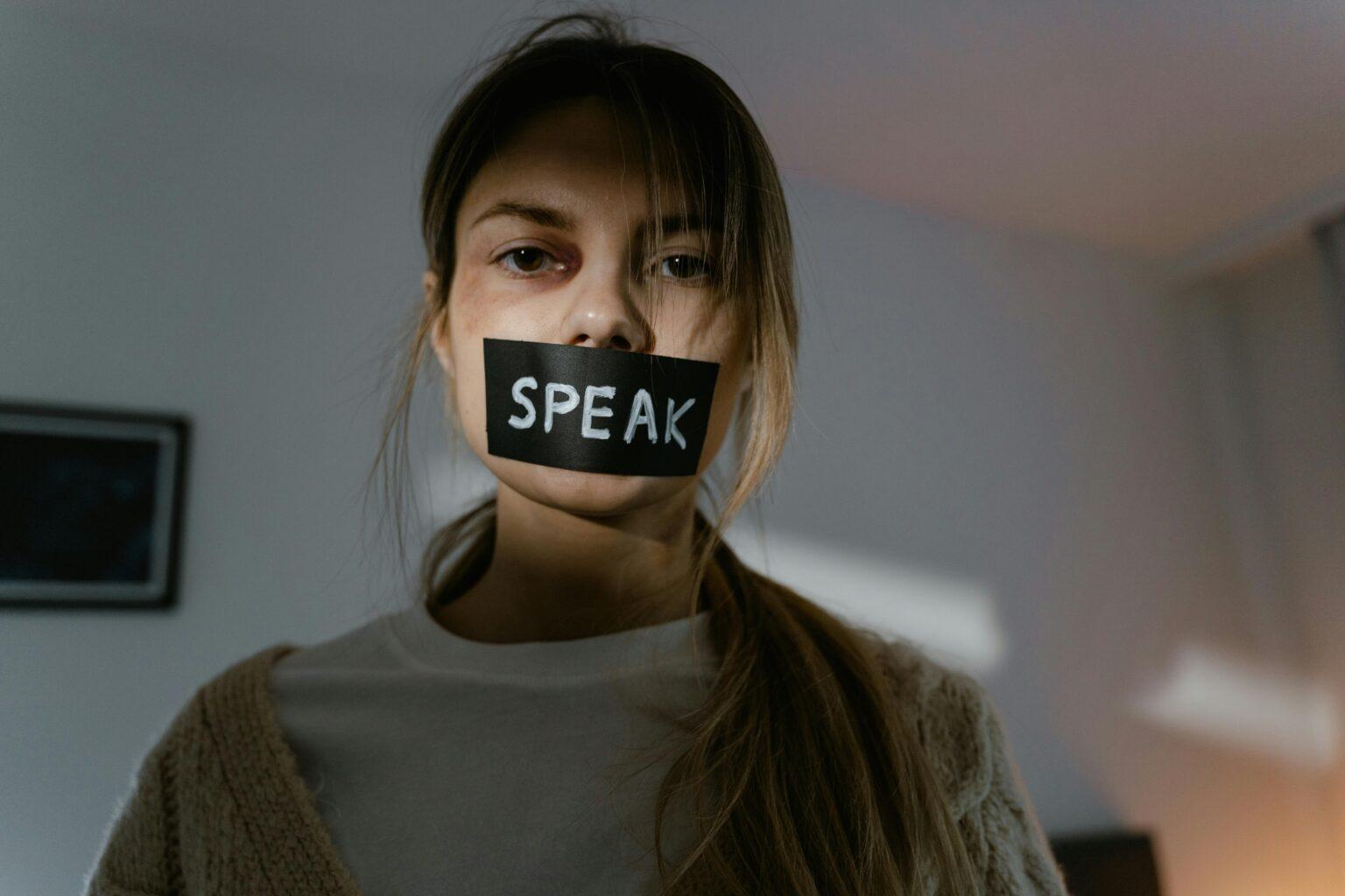 Woman with 'speak' tape over mouth.