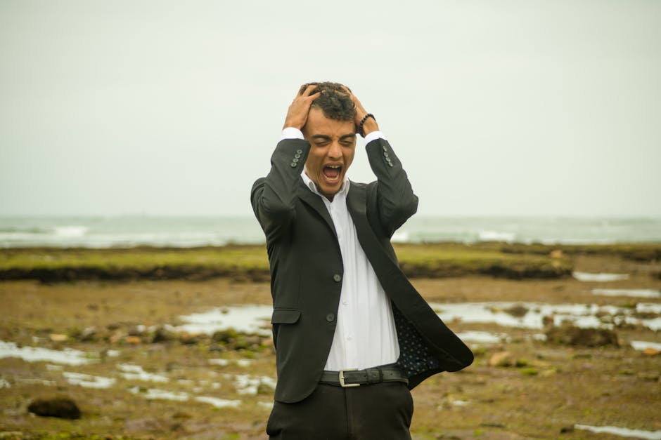 Homme d'affaires stressé en costume, tenant sa tête face à une côte rocheuse agitée, illustrant la gestion du stress et la vi