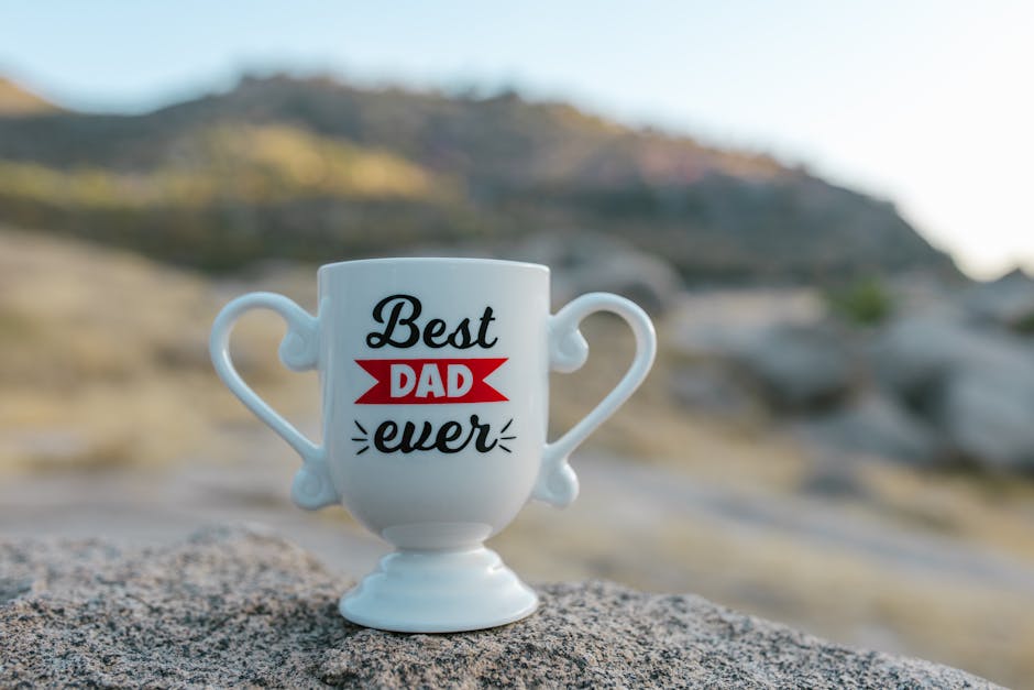 Excitement vs Contentement : quel est le secret du bonheur durable A white trophy-shaped mug with 'Best Dad Ever' text placed on a rock in a natural outdoor setting.