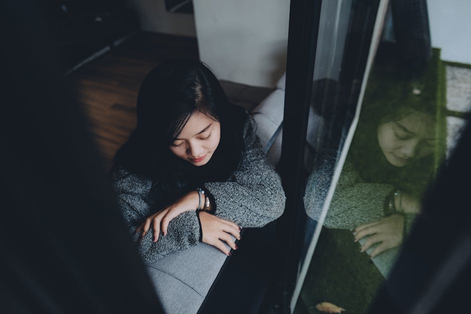 Person sitting alone by a window after a breakup, reflecting on emotional healing