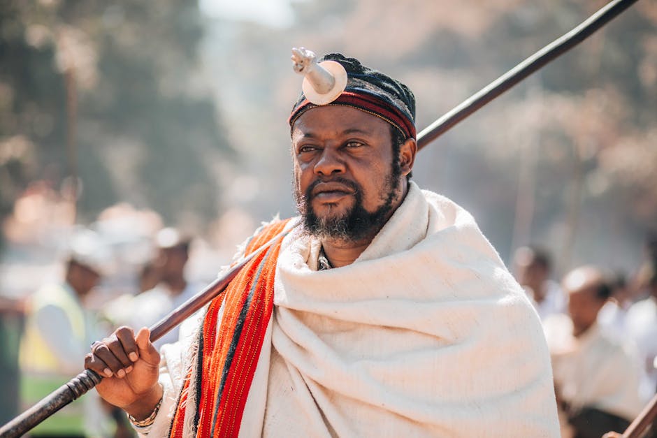 Sagesse et connaissance : les forces de caractère qui différencient les leaders A man in traditional African attire holding a spear during a vibrant cultural festival outdoors.
