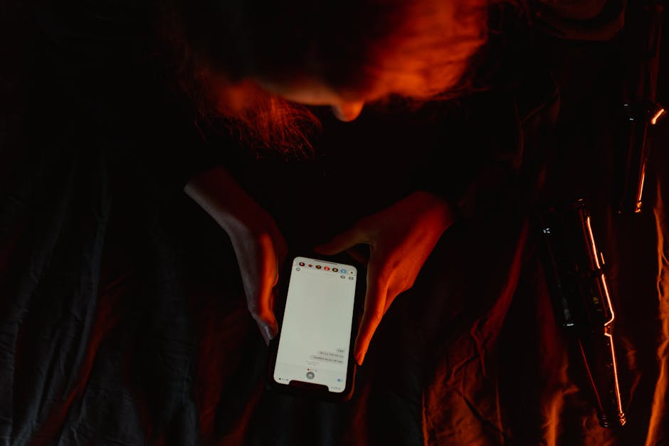 Jeune adulte absorbé par son smartphone dans une pièce sombre