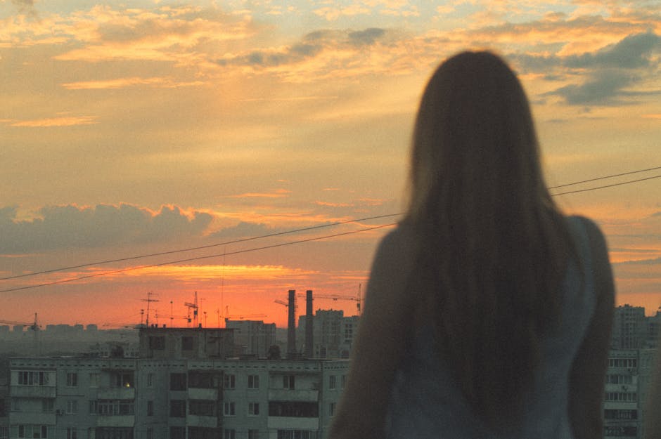 Person standing at a window looking out over a city skyline at sunrise