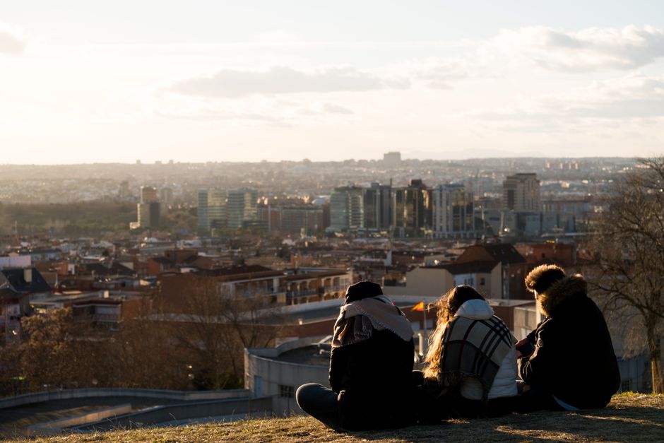 Capital psychologique et espoir : le moteur caché de la performance au travail Three people sitting on a hill enjoying the view of Madrid's skyline at sunset.