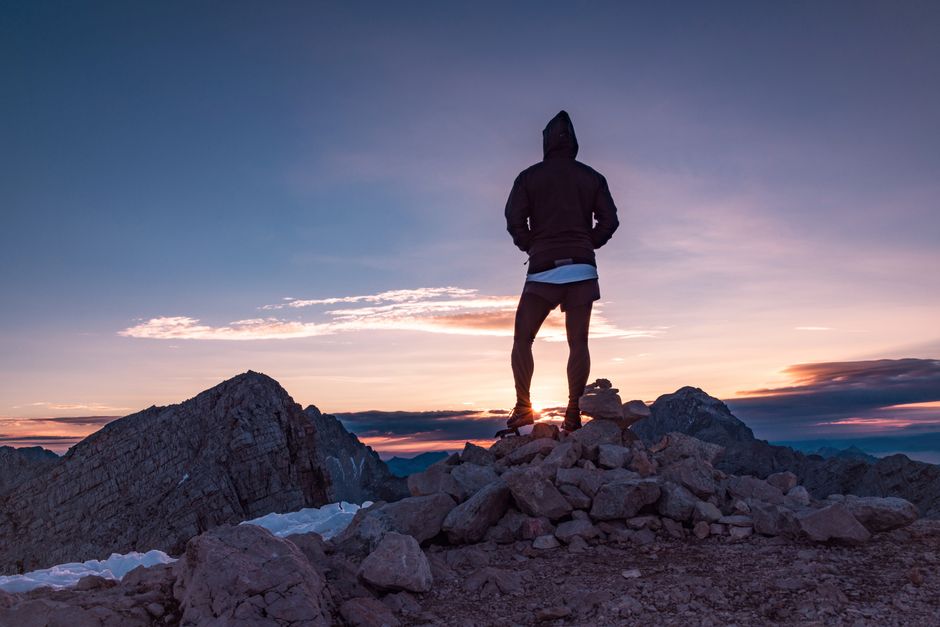 Person standing on a mountain summit at sunrise, symbolizing achievement and fulfillment