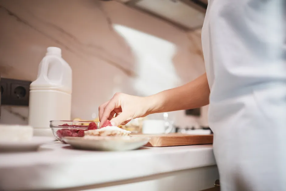 A close-up of a person preparing a raspberry dish on a kitchen counter.