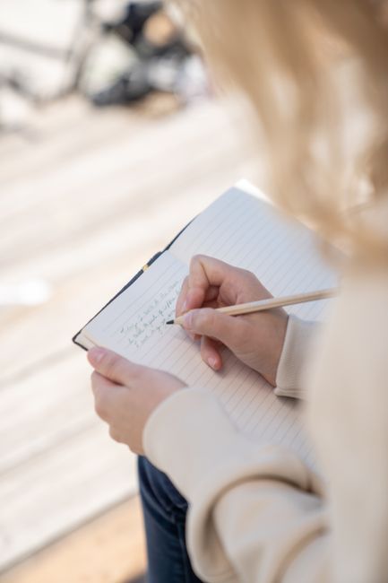 A close-up of a person writing in a notebook outdoors on a sunny day, capturing a moment of inspiration.