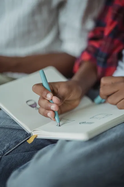 A close-up view of a person sketching on a notebook using a pen, showcasing creativity and focus.