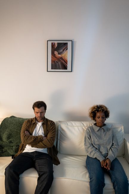 A couple experiencing tension, sitting apart on a sofa indoors.