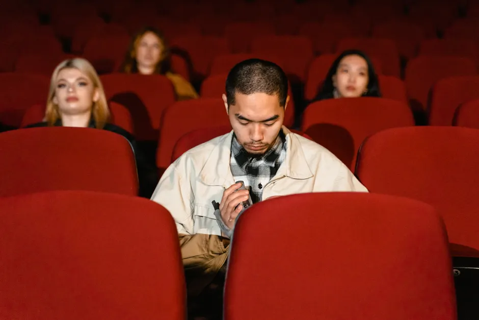 A diverse group seated in a movie theater, watching seriously.