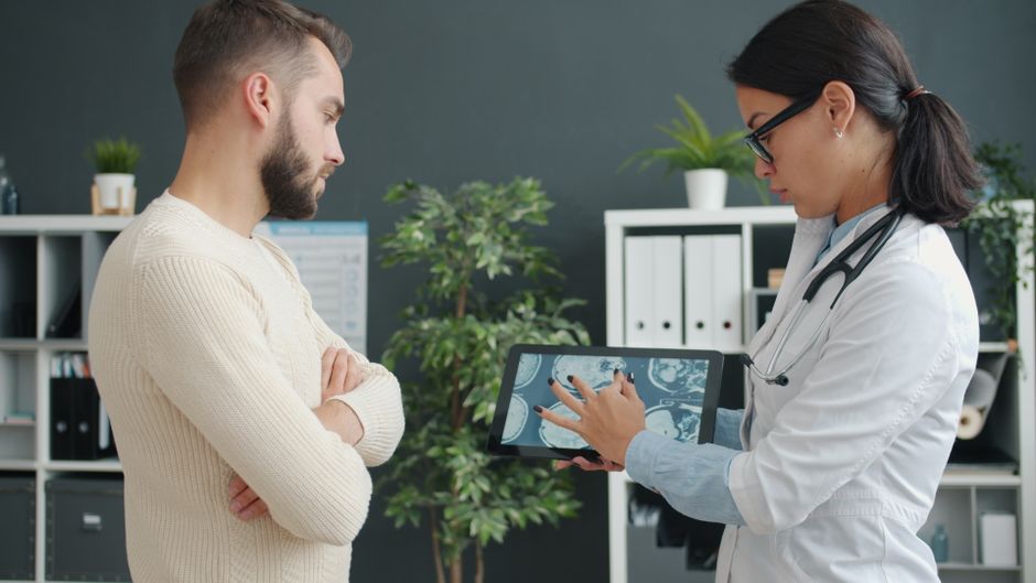 A doctor shows MRI scan to a worried patient using a tablet in a modern clinic.