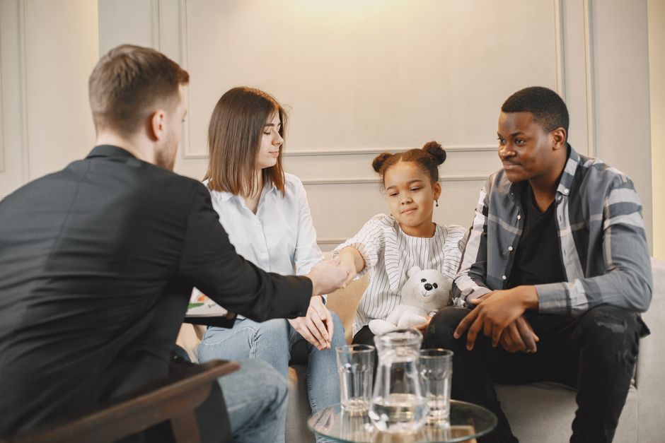 A family in a thoughtful counselling session with a professional in a modern setting.