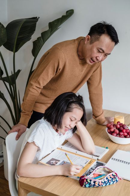 A father helps his daughter with homework in a cozy indoor setting, featuring a supportive learning environment.