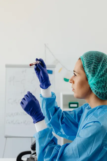 A female scientist analyzing a blood sample in a laboratory environment, wearing PPE.