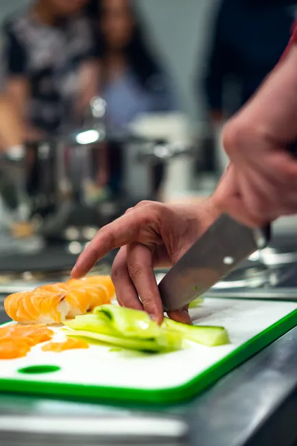 A focused image of a person slicing vegetables on a green-edged cutting board in a kitchen.