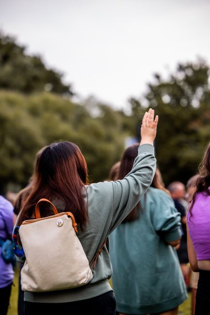 A group of adults outdoors, one person raising a hand, suggesting engagement or participation.
