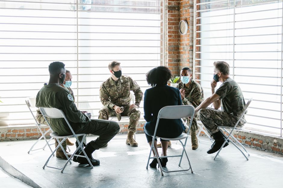 A group therapy session with soldiers in military uniform and face masks indoors.