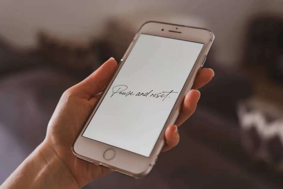 A hand holding a smartphone with a motivational quote on the screen, suggesting reflection.