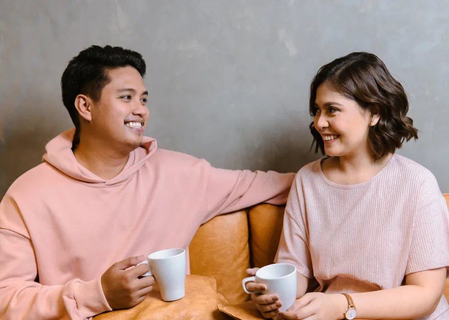 A happy couple sharing a moment with coffee cups, indoors in a cozy setting.