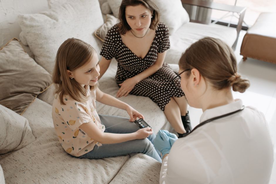 A healthcare provider assists a child with a diabetes check-up at home.