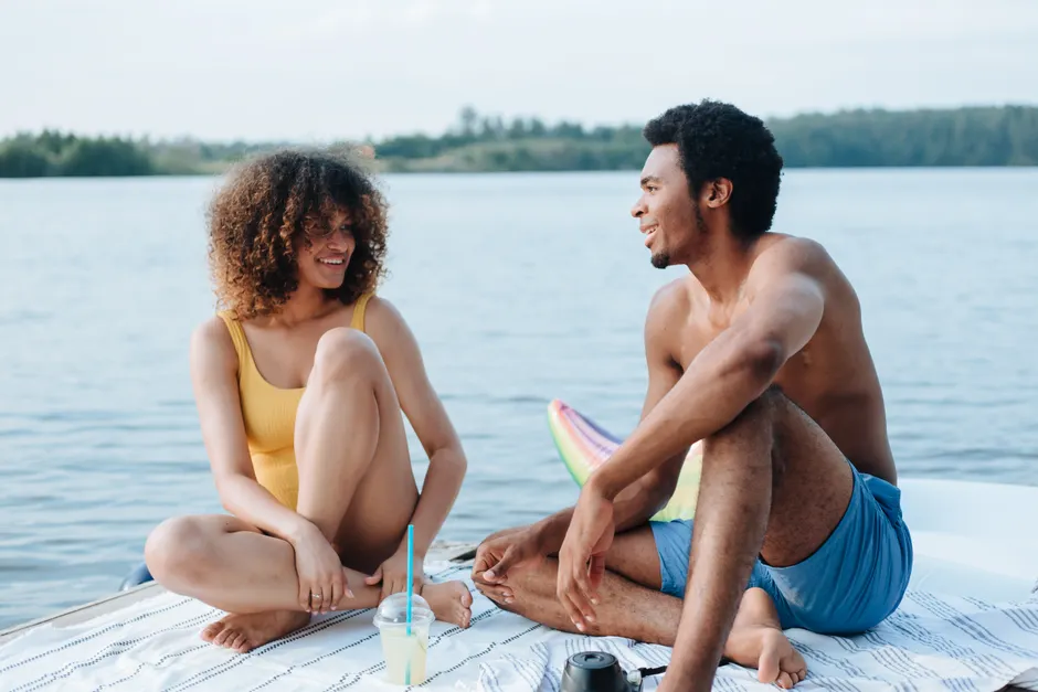 A joyful moment of a young couple relaxing and talking by the lake on a sunny day.
