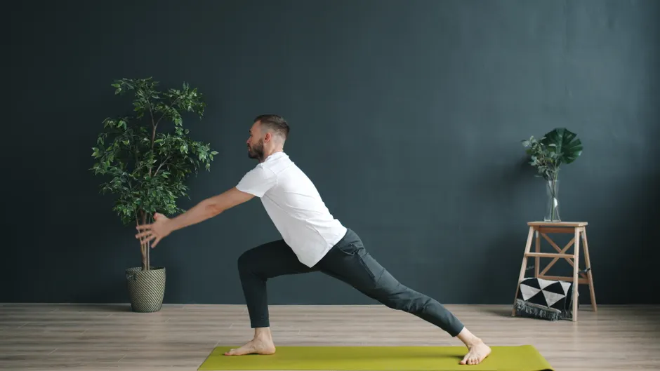 A man practicing yoga indoors on a green mat, focusing on balance and flexibility.