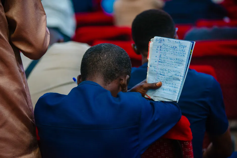 A man seated in a church holding a notebook, capturing moments of devotion and prayer.