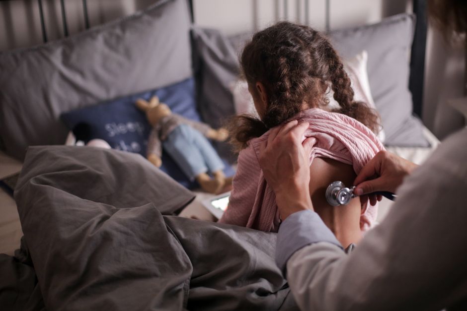 Trouble factice imposé à autrui : reconnaître la maltraitance médicale sans accuser à tort A pediatric doctor checks a child's back with a stethoscope in a cozy bedroom setting.