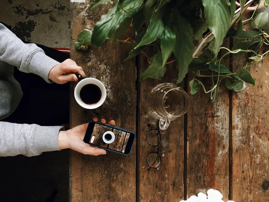 Gérer l’impulsivité : 6 stratégies pour créer un délai avant l’acte A person enjoys coffee and uses a smartphone, surrounded by greenery. Perfect for lifestyle themes.